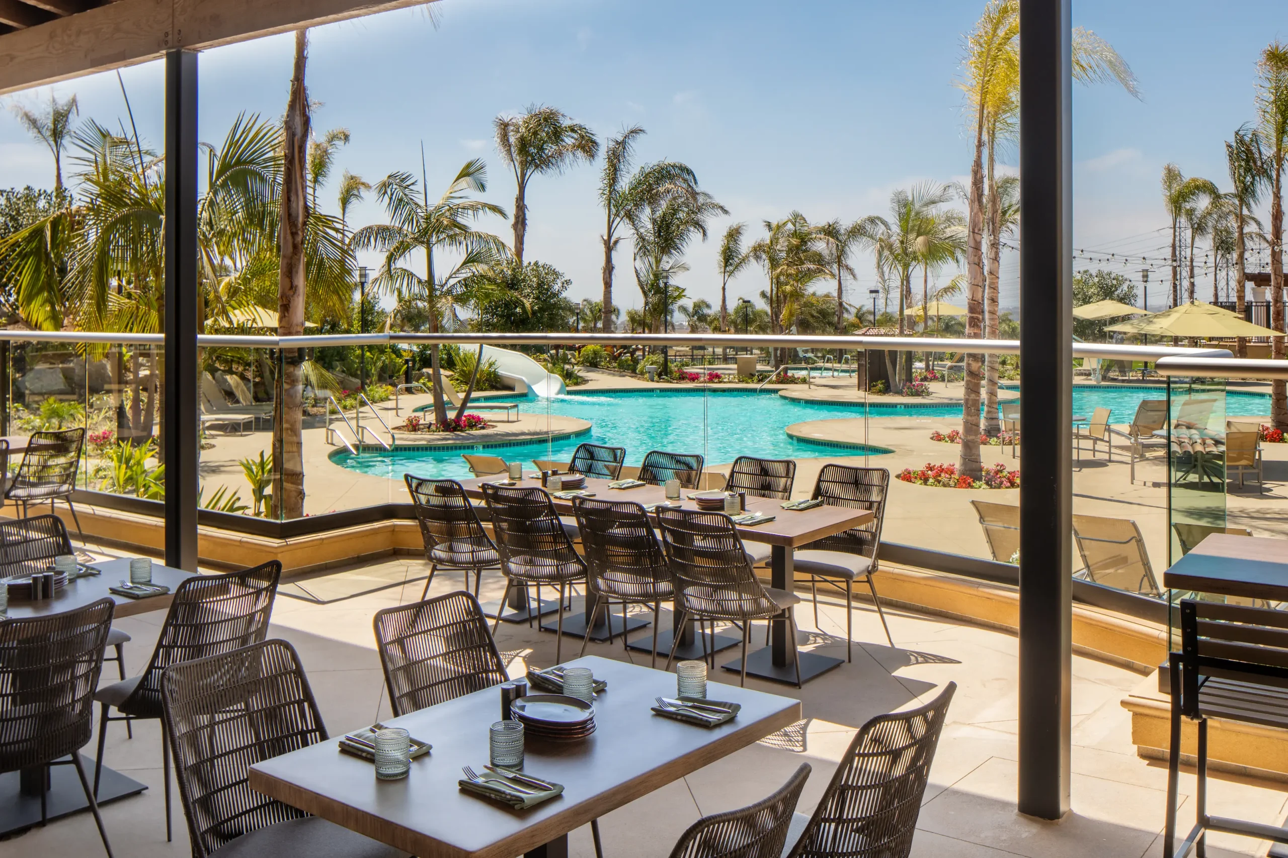 Patio dining seating with overview of hotel swimming pool and palm trees
